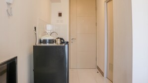 A narrow hallway with a black refrigerator, a white kettle, and a white phone on the wall. A door is visible at the end of the hallway. - Brand New Studio At Tokyo Riverside Pik 2 Apartment (Teluknaga)