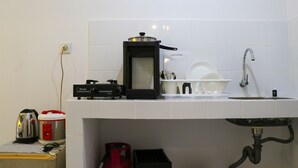 Una cocina con un lavamanos blanco, una cafetera, una olla arrocera y un hervidor sobre la encimera.