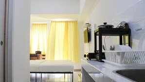 Una habitación de hotel moderna con kitchenette, una cama, una mesita de noche y un ventanal con cortinas amarillas.