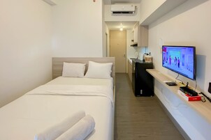 Quarto de hotel com uma cama, televisão sobre um suporte e uma escrivaninha com um computador e uma caixa vermelha.