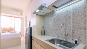 A compact hotel room with a kitchenette, a bed with a white comforter, and a window with curtains. - Simply Look Studio At Evenciio Margonda Apartment (Depok)