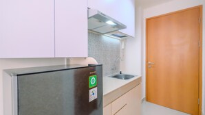 A compact kitchen with white cabinets, a stainless steel refrigerator, a tiled backsplash, and a wooden door. - Simply Look Studio At Evenciio Margonda Apartment (Depok)