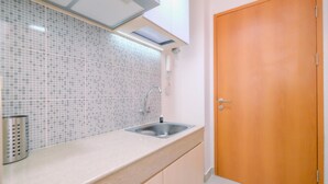 A kitchen with a tiled backsplash, a stainless steel sink, and wooden cabinets. - Simply Look Studio At Evenciio Margonda Apartment (Depok)
