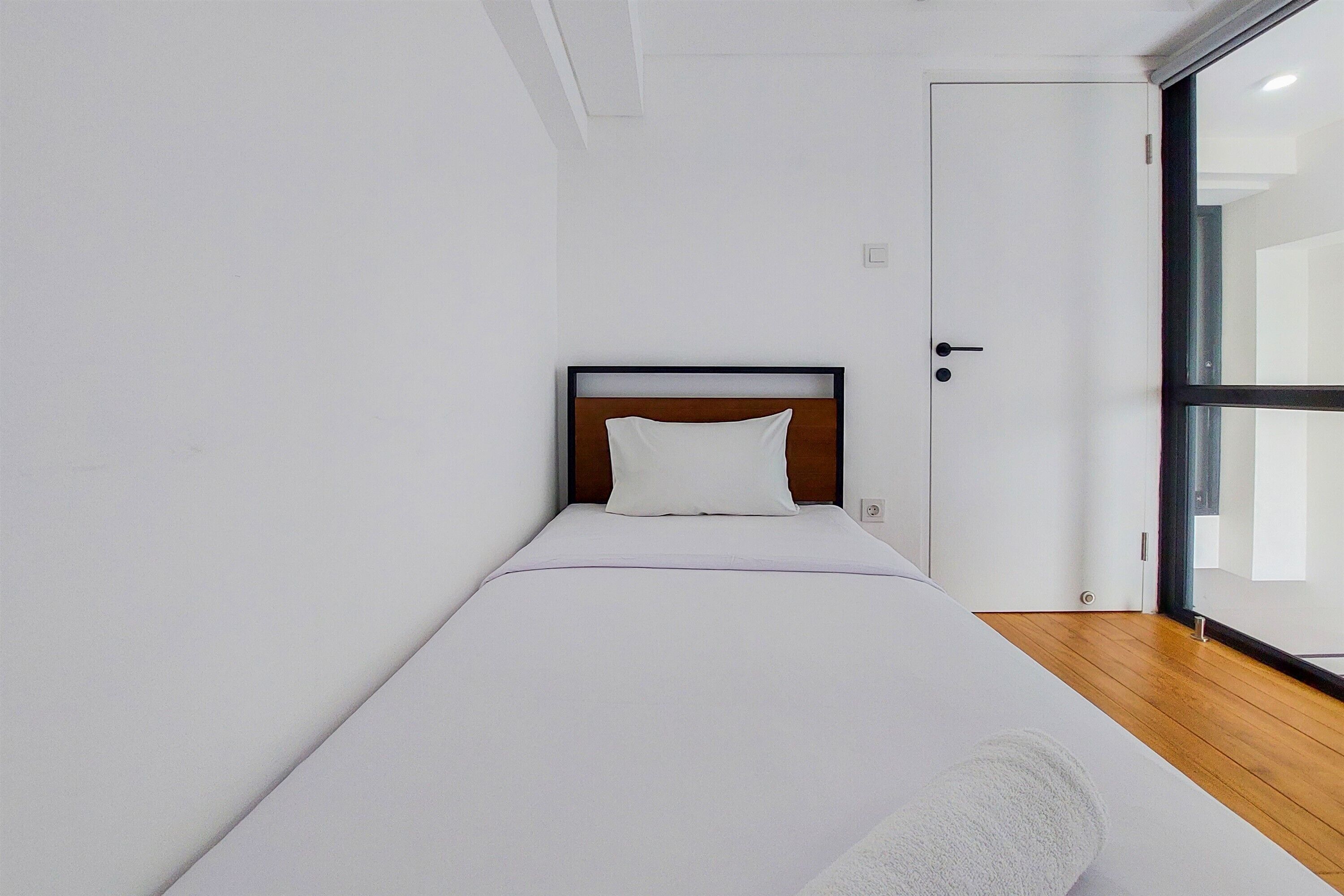 Una cama individual con cabecera de madera y ropa de cama blanca en una habitación con paredes blancas y suelo de madera.