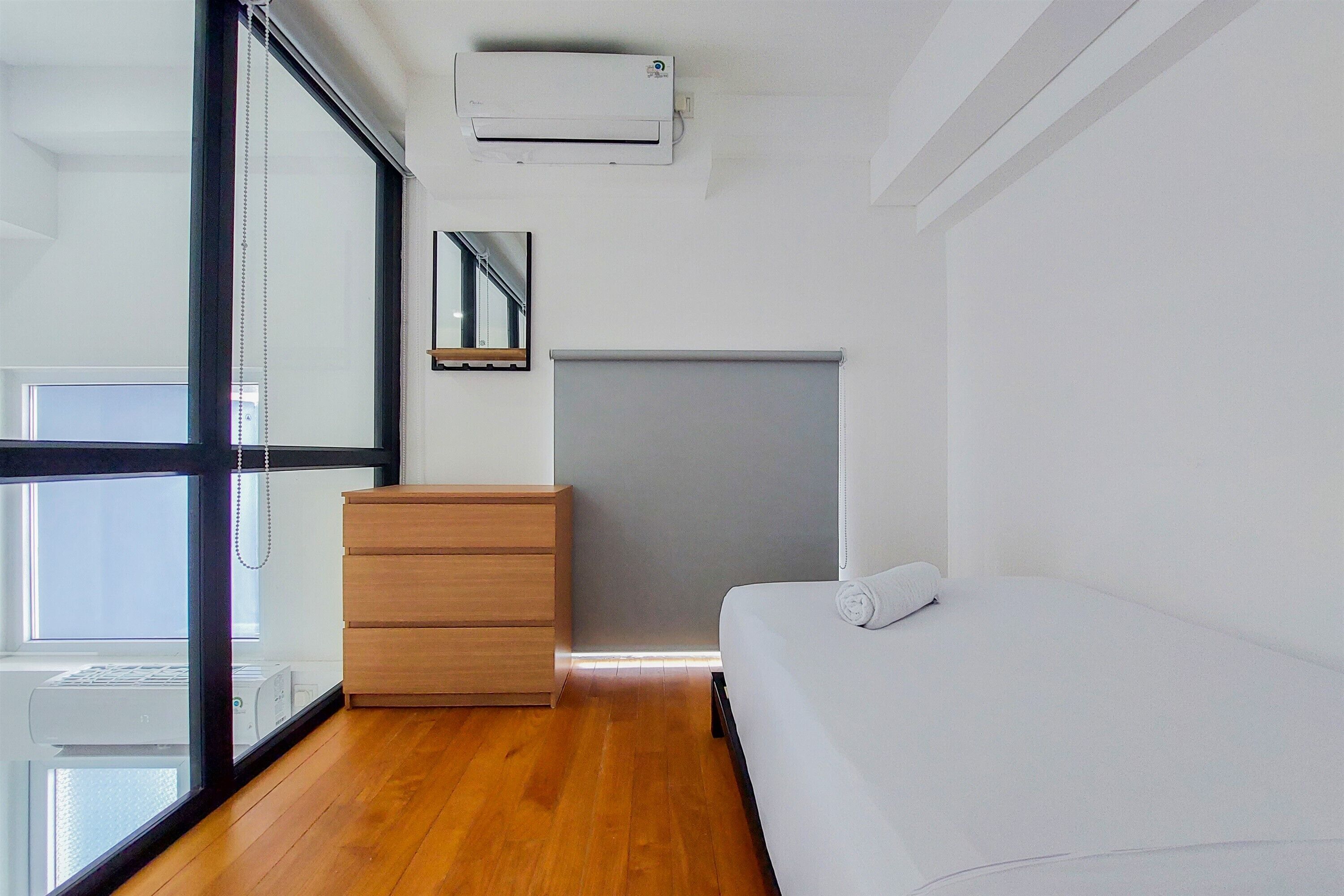 Un dormitorio moderno con un aparador de madera, una cama, un mueble gris y un amplio ventanal con persianas.