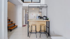 Una cocina compacta con una barra de madera, dos taburetes, un perchero y un refrigerador.