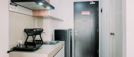 A compact kitchen with a built-in microwave, a small refrigerator, and a sink with a black tray.