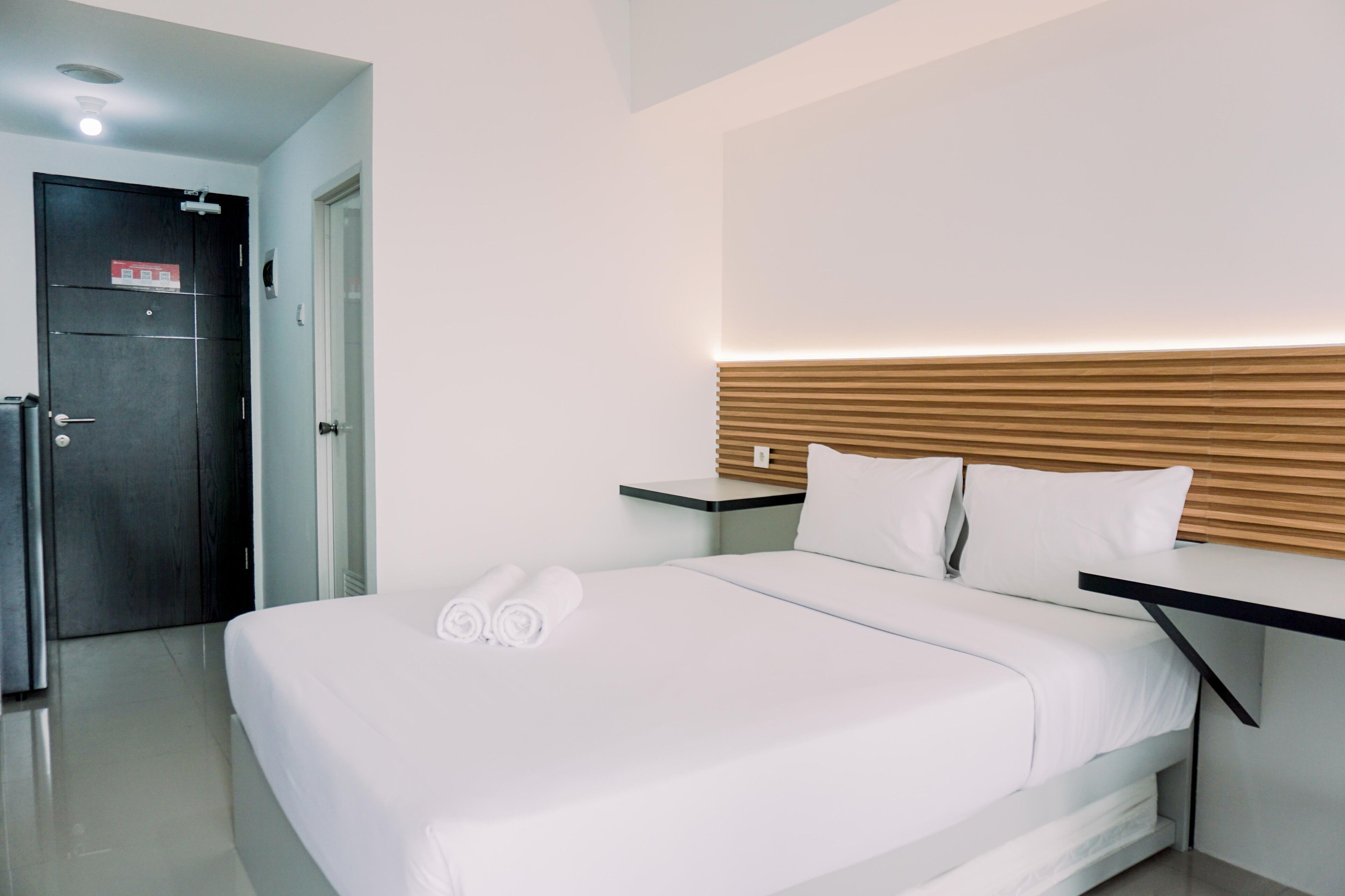 A modern hotel room with a neatly made bed, a wooden headboard, and a small bedside table.