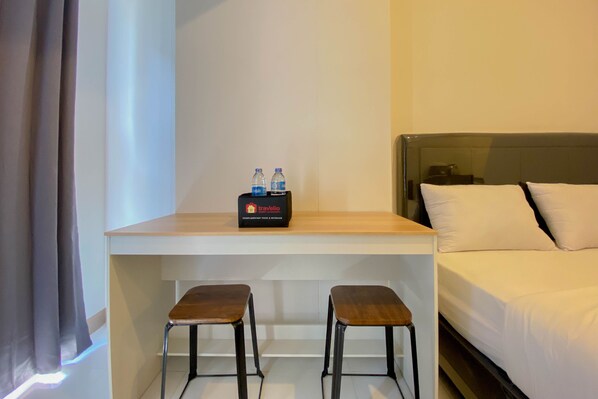 Una habitación de hotel con una cama, un escritorio con dos taburetes y un minibar con agua embotellada.