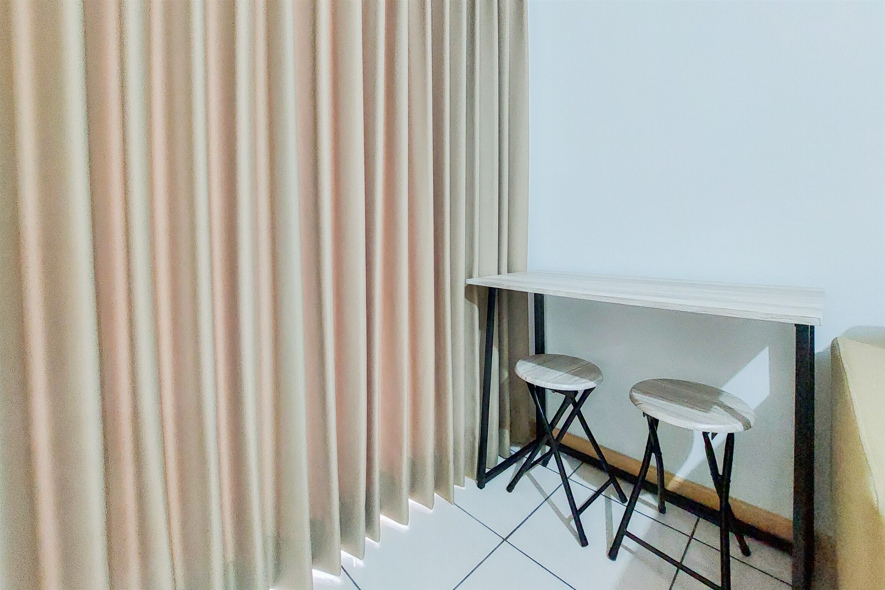 Une pièce avec une table blanche et deux tabourets, un rideau et un sol carrelé.