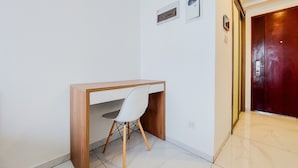 Un espacio de oficina pequeño y moderno con un escritorio de madera y una silla blanca, una unidad de aire acondicionado instalada en la pared y una puerta con manija metálica.