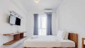 Un dormitorio moderno con cama, televisor montado, estante empotrado y ventana con cortinas.