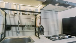 A modern kitchen with a stainless steel sink, a black stove, and a hanging pot rack. - Homey And Warm Studio Amazana Serpong Apartment (South Tangerang)
