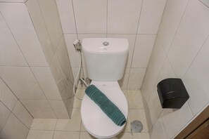 A bathroom with a white toilet, a towel on the seat, and a black trash bin. - Homey And Warm Studio Amazana Serpong Apartment (South Tangerang)