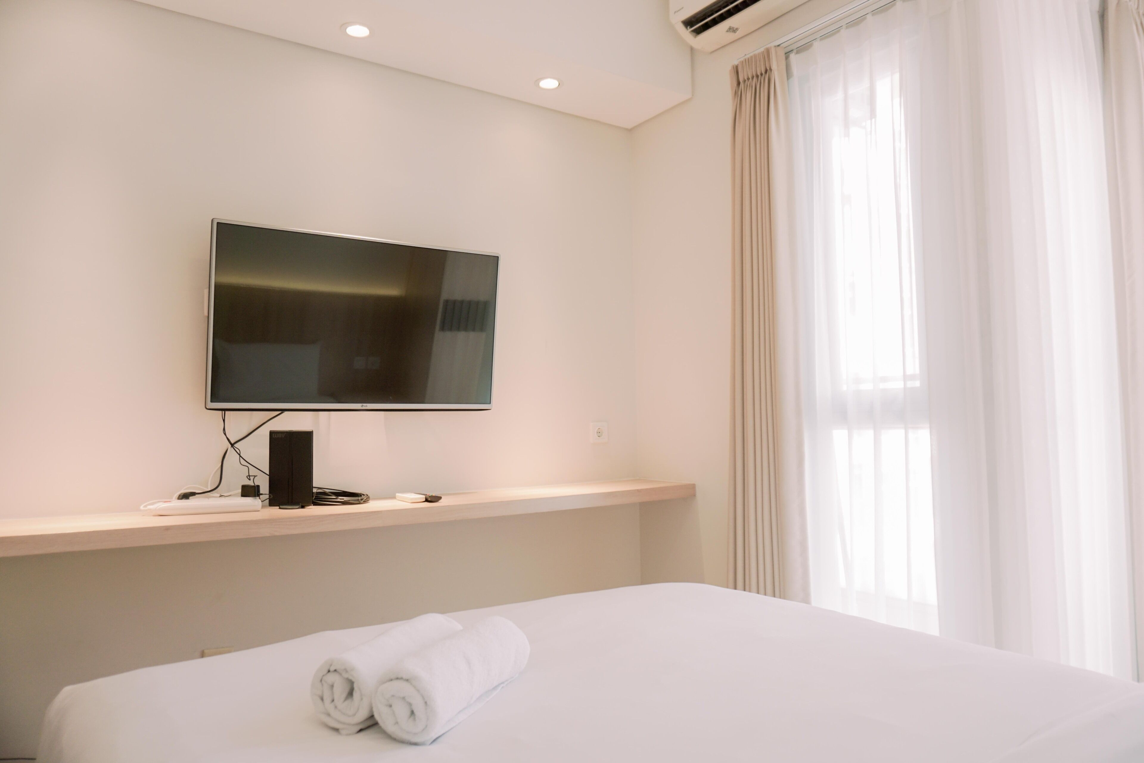 Une chambre d’hôtel avec un lit, un téléviseur fixé au mur et une fenêtre avec des rideaux.