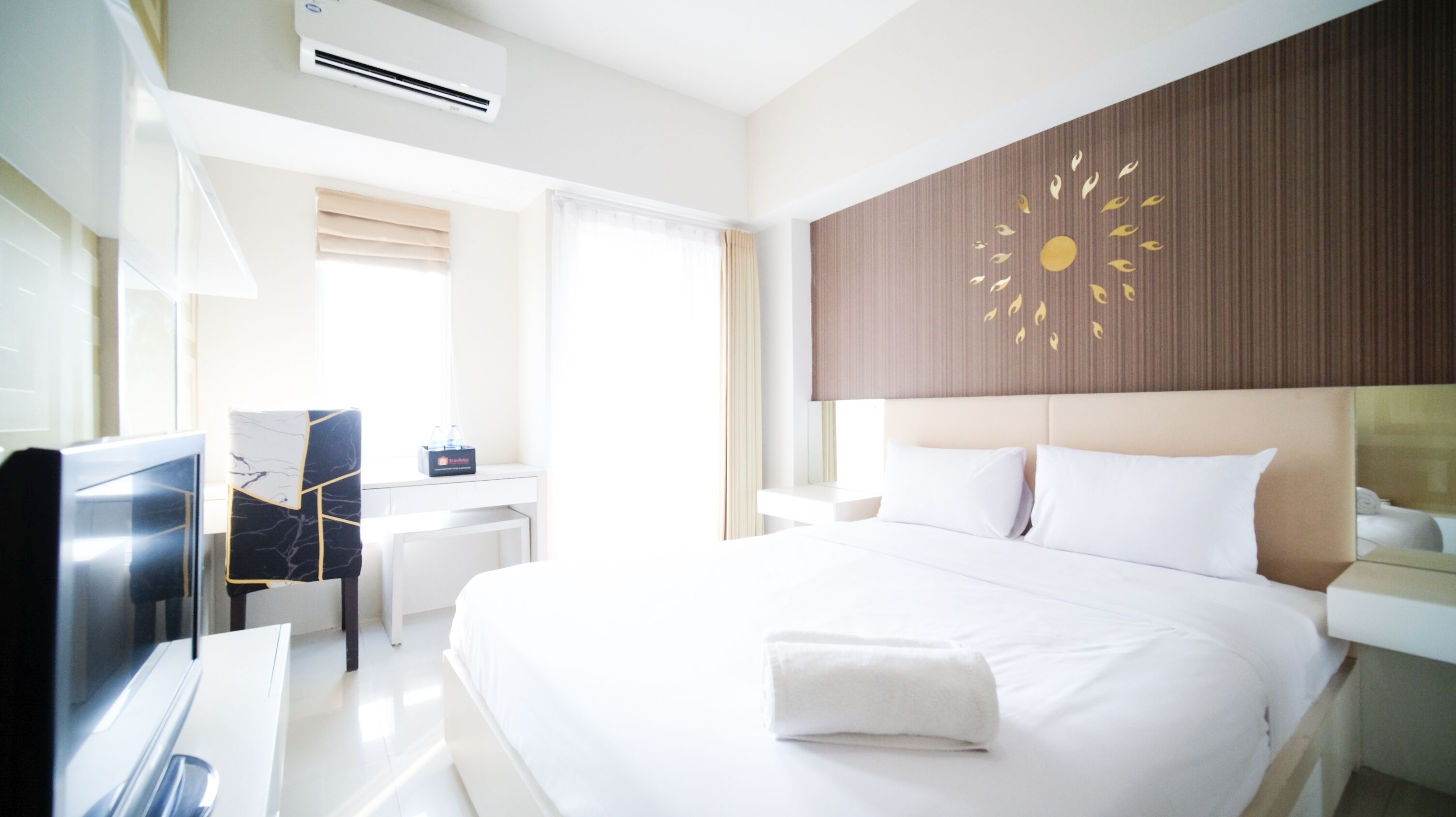Habitación de hotel con una cama grande, un escritorio, una silla y una pared con un diseño de sol.