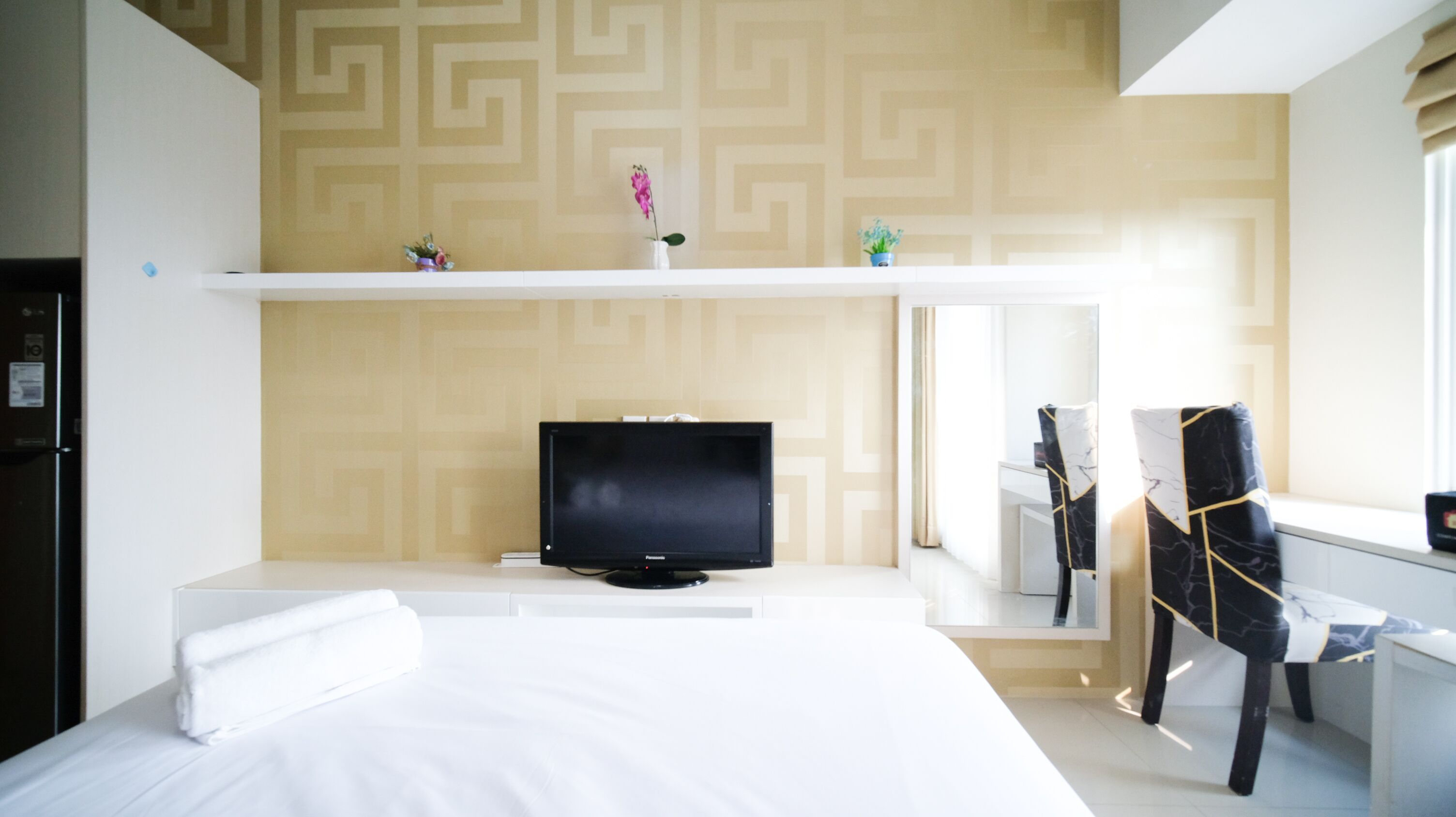 A hotel room with a bed, a television, a desk with a chair, and a mirror.