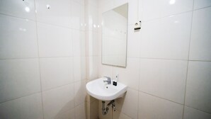 Une salle de bain avec des carreaux blancs, un lavabo, un miroir et un robinet.