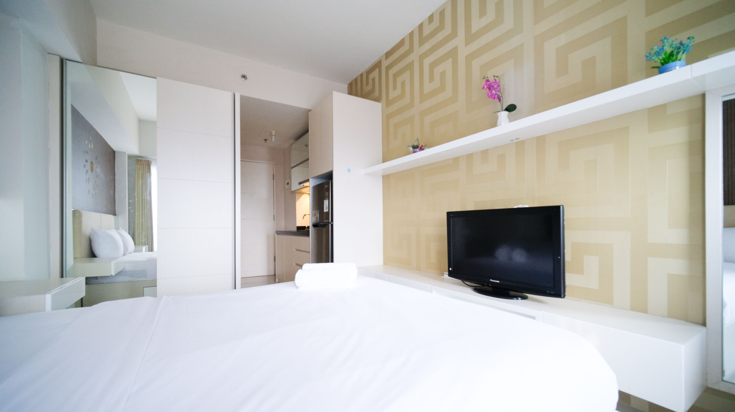 A modern hotel room with a large bed, a flat-screen TV, a walk-in closet, and a kitchen area.