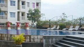 A swimming pool with steps leading down to the water, surrounded by lounge chairs and a potted plant. - Homey And Simply Look Studio Belmont Residence Puri Apartment (Jakarta)