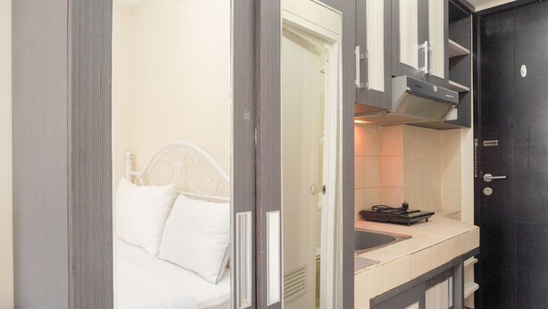 A compact hotel room with a bed, a small kitchenette, and a dark door. - Homey And Simply Look Studio Belmont Residence Puri Apartment (Jakarta)
