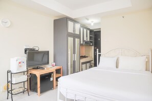 A hotel room with a bed, a desk with a computer, a television, and a kitchenette. - Homey And Simply Look Studio Belmont Residence Puri Apartment (Jakarta)