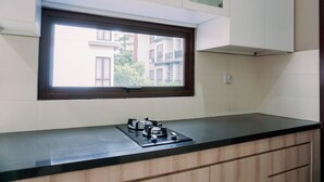 A kitchen with a gas stove, a window with a view of buildings, and white cabinets. - Best Deal And Comfortable 2Br Asatti Apartment (Pagedangan)