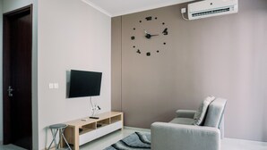 A modern living room with a flat-screen TV, a grey sofa, a wooden entertainment unit, and a wall clock. - Best Deal And Comfortable 2Br Asatti Apartment (Pagedangan)