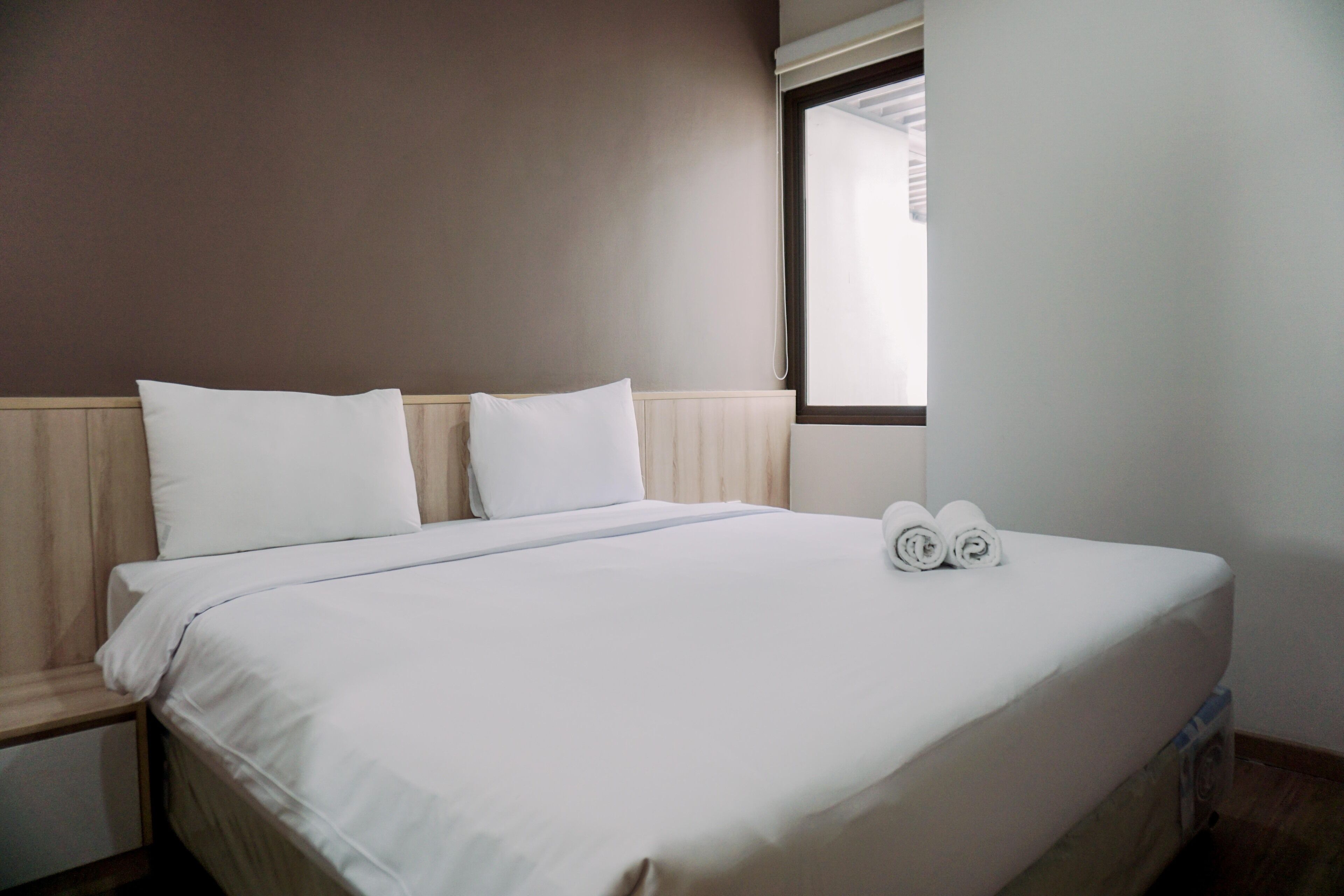 A neatly made bed with white linens and two rolled towels on the bed.