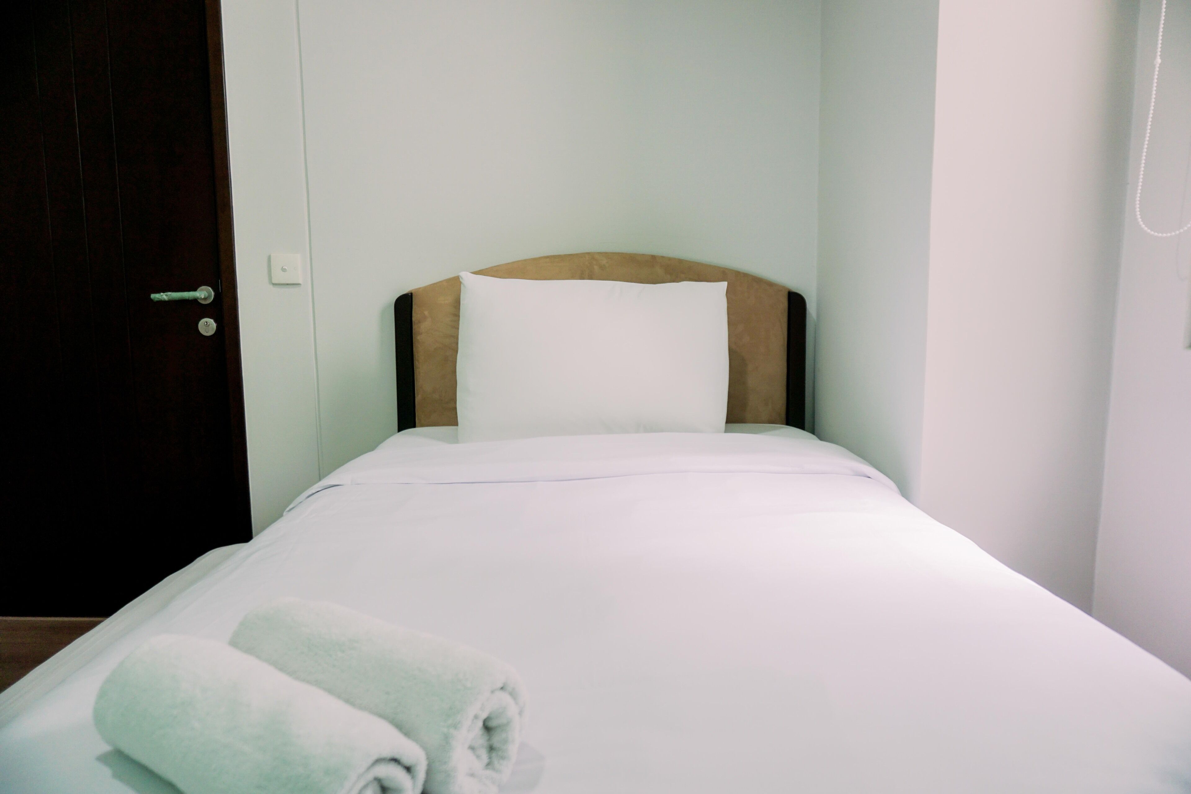 A neatly made bed with white linens and a rolled towel on the side.
