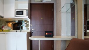A compact kitchen with a microwave, sink, and cabinets. A small table with a bag labeled "Travelio" is in front of a door.