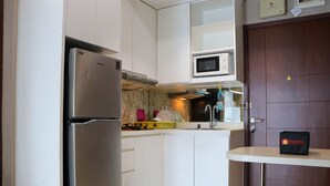 A compact kitchen with white cabinets, a stainless steel refrigerator, a microwave, and a small table with a bag labeled "travelio".