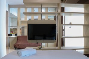 Ein modernes Hotelzimmer mit einem großen Bett, einem flachbildfernseher an einer Holzverkleidung, einem Sessel mit brauner Sitzfläche und einem großen Fenster, das für natürliches Licht sorgt.