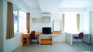 Ein Hotelzimmer mit Schreibtisch, zwei Stühlen, Fernseher und einem Fenster mit Vorhängen.
