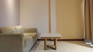 Um quarto com um sofá bege, uma mesa branca e uma cortina.