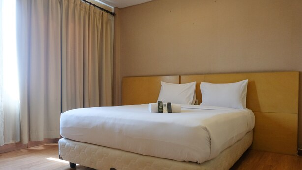 Quarto de hotel com uma cama grande, cortinas bege e piso de madeira.