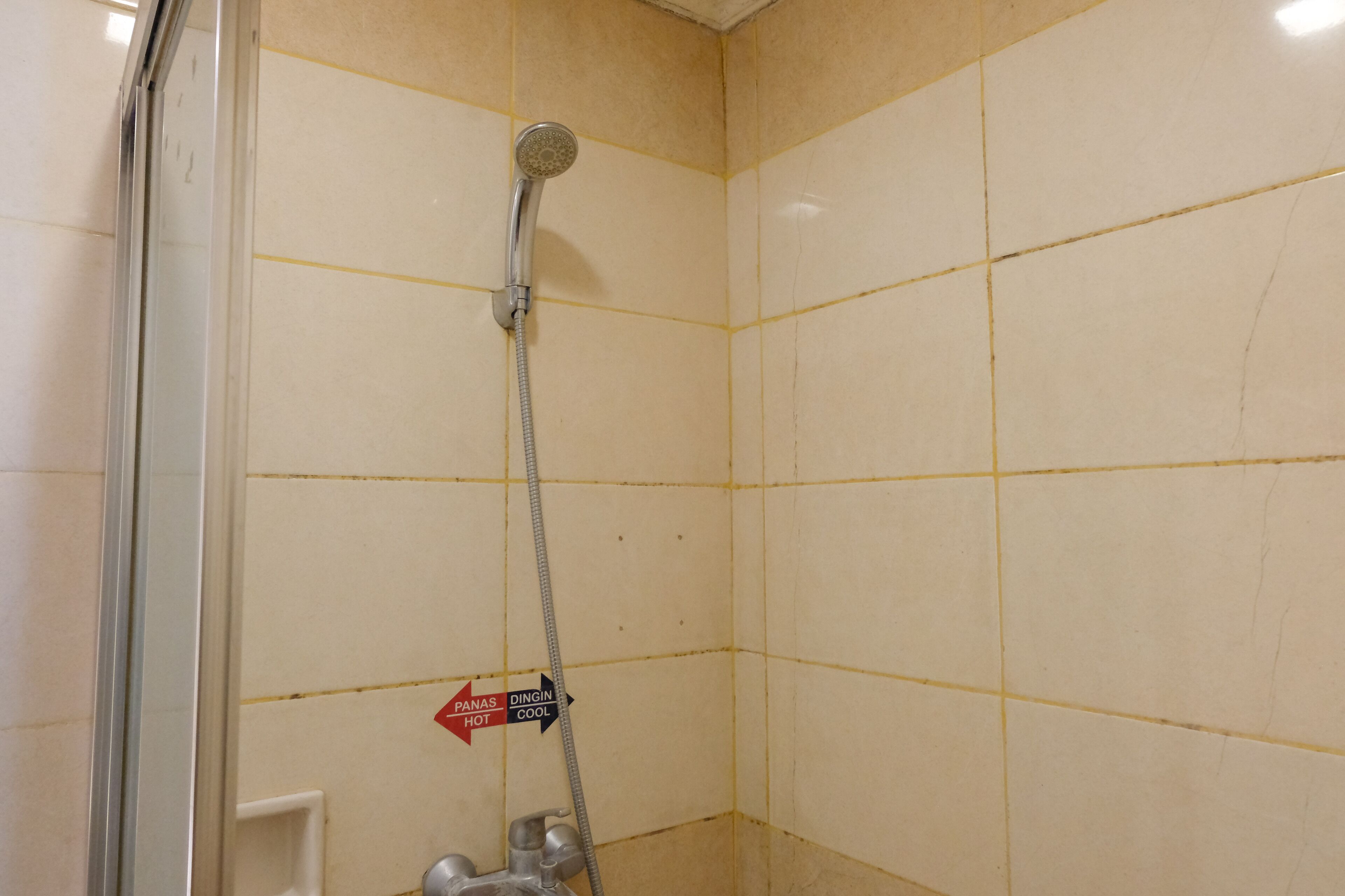 Une salle de bain avec des murs carrelés de couleur beige, une douche équipée d’un pommeau de douche à main et un panneau indiquant les options d’eau chaude et d’eau froide.