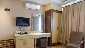 Quarto de hotel com televisão de tela plana, uma escrivaninha com computador, uma cadeira, guarda-roupa e ar condicionado.