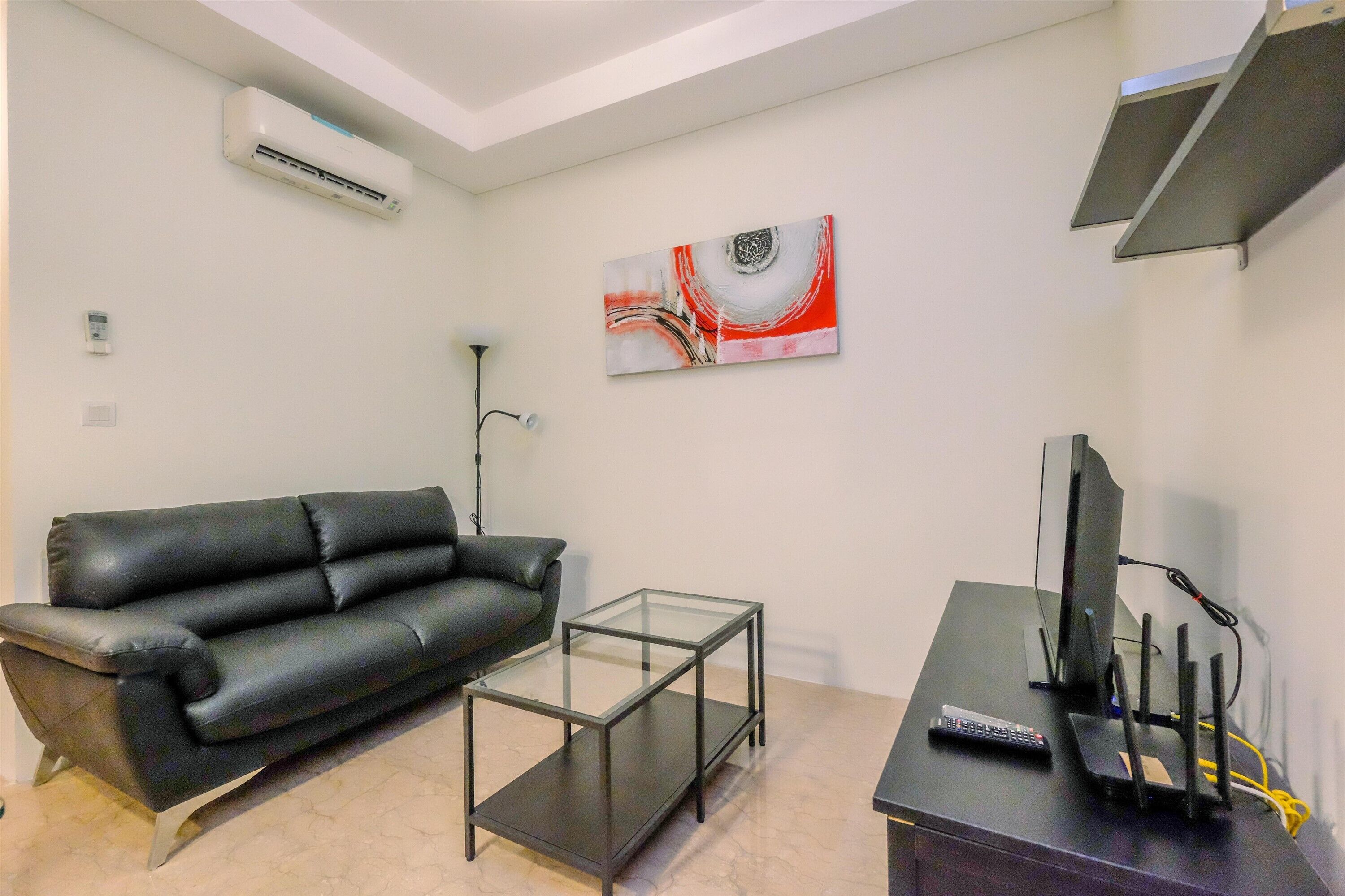 Uma sala de estar com sofá de couro preto, mesa de centro de vidro, televisão de tela plana e um quadro na parede.