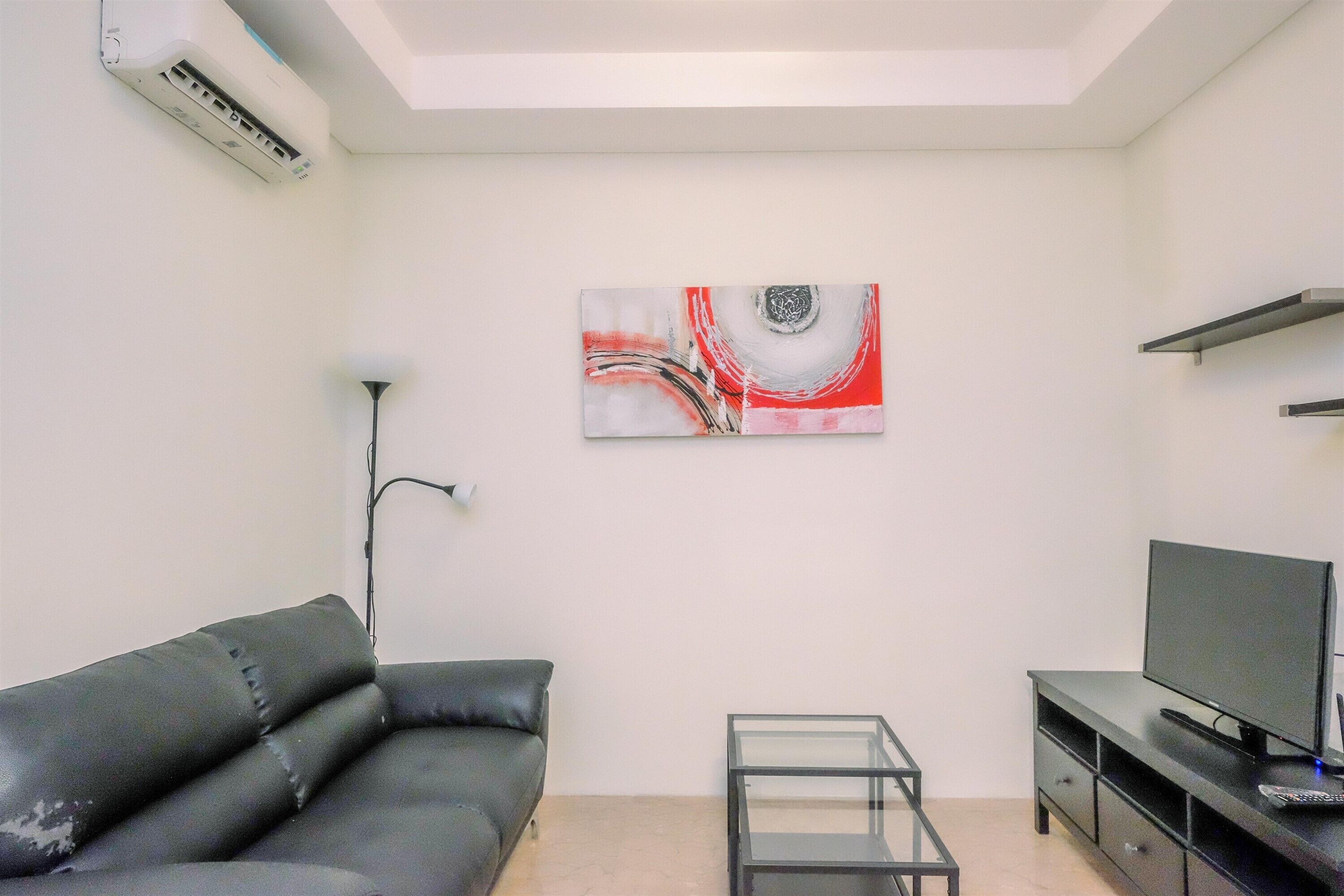 A living room with a black leather sofa, a glass coffee table, a flat-screen TV on a black stand, and a modern abstract painting on the wall.