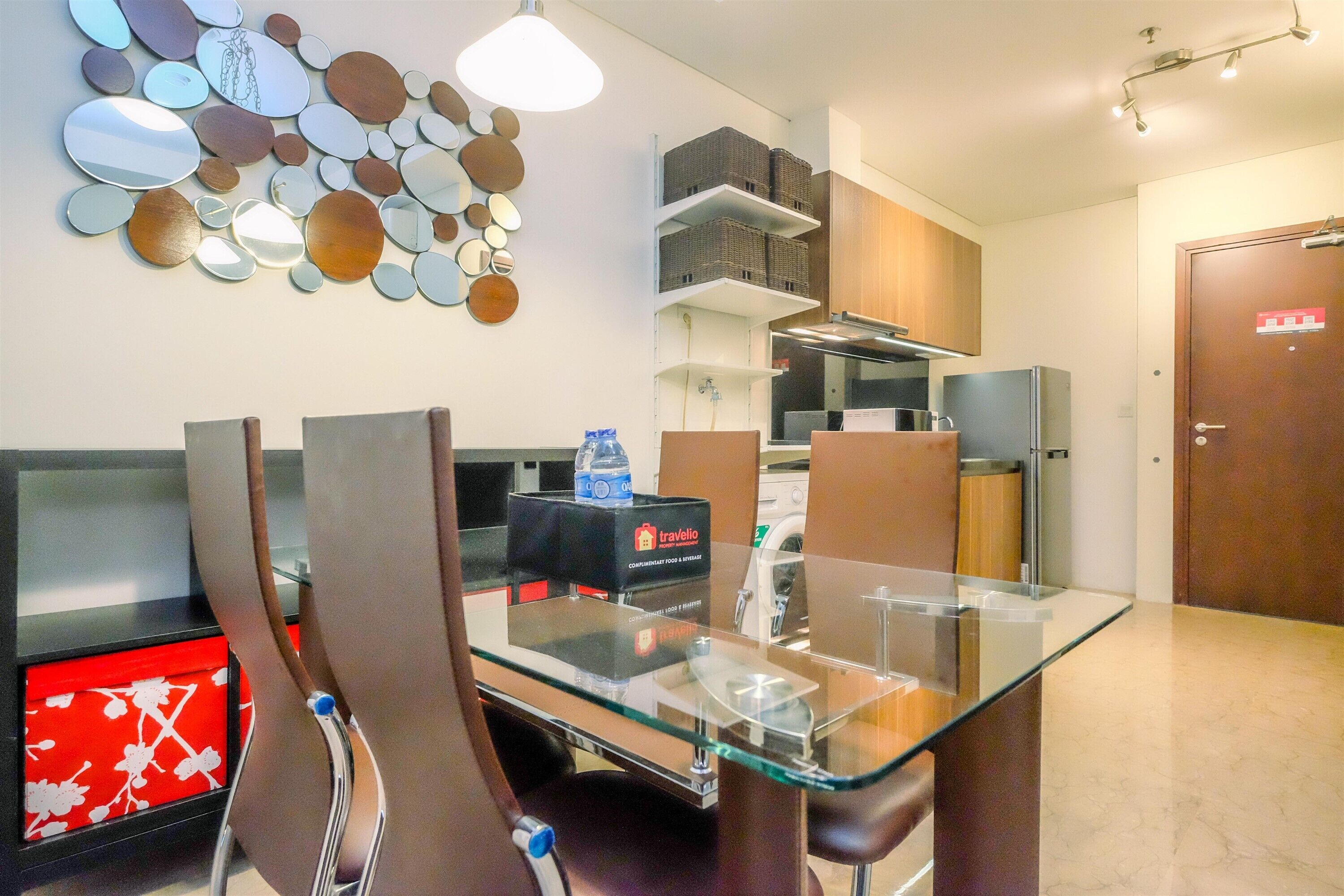 A modern kitchen with a glass dining table, stainless steel appliances, and a wall-mounted mirror art piece.