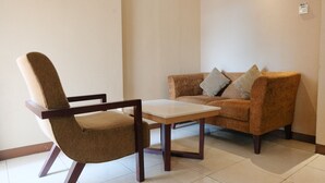 Una habitación con un sillón marrón, una mesa blanca y un sofá marrón con cojines.