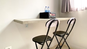 A small room with a wooden shelf holding a box labeled 'travelio' and two bottles of water. There are two black chairs in the foreground. - Best Deal And Cozy Studio At Apartment Transpark Juanda Bekasi Timur (Bekasi)
