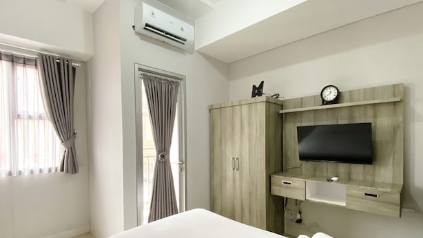 A hotel room with a bed, a TV mounted on the wall, a wardrobe, and an air conditioning unit. - Best Deal And Cozy Studio At Apartment Transpark Juanda Bekasi Timur (Bekasi)
