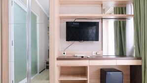 Une chambre moderne avec un bureau en bois, un téléviseur à écran plat fixé au-dessus, un petit pouf noir et un rideau vert.
