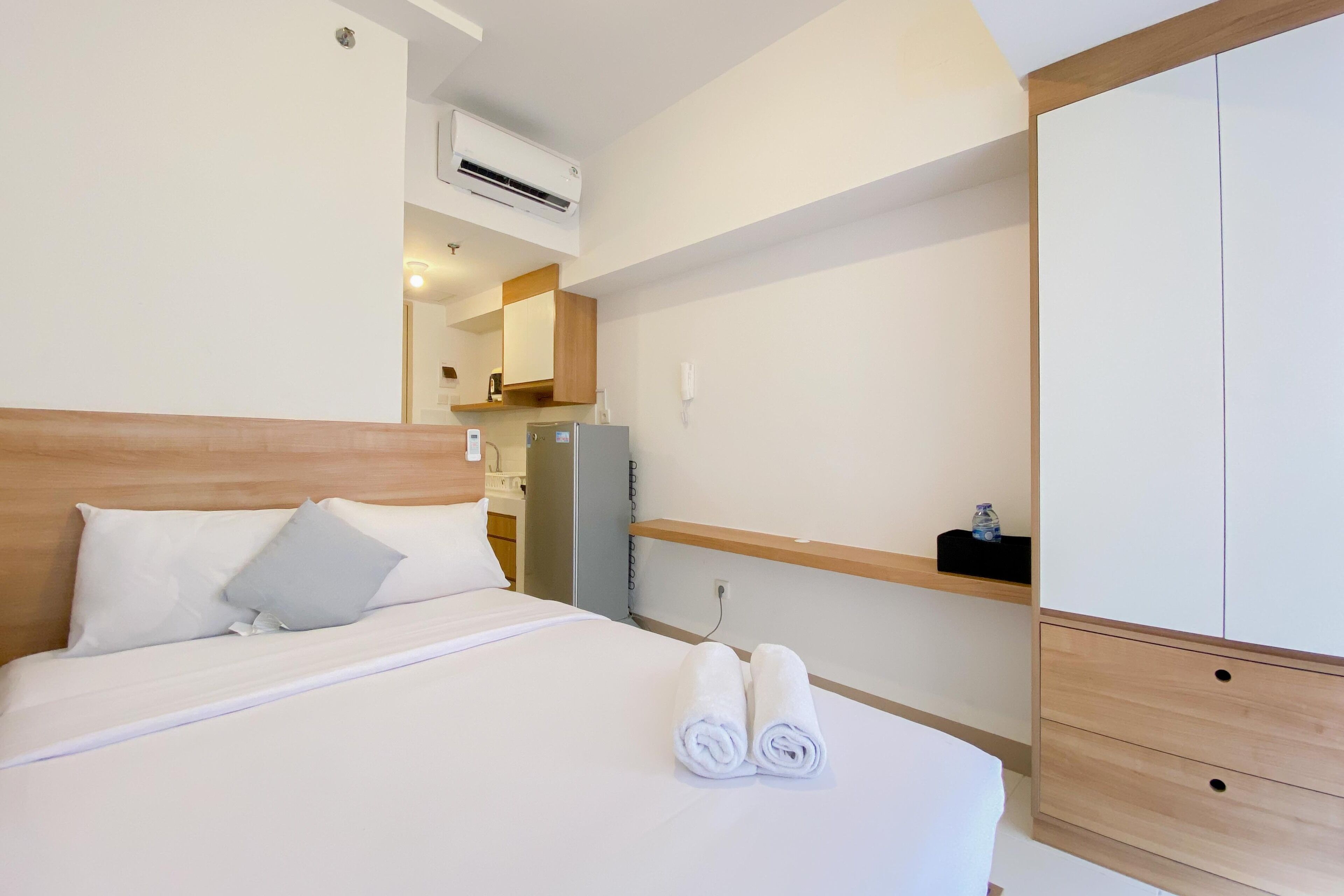A hotel room with a bed, a wardrobe, a small kitchenette, and an air conditioning unit.