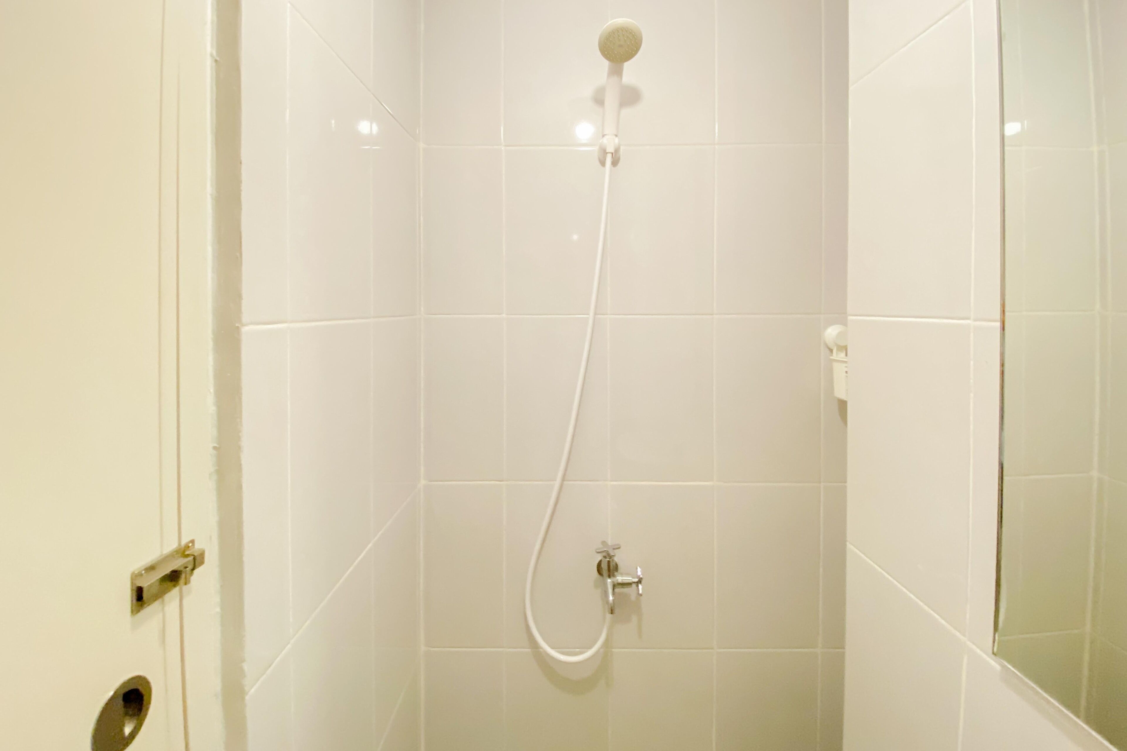 Un bagno con piastrelle bianche, una doccia con soffione manuale e una porta con maniglia.