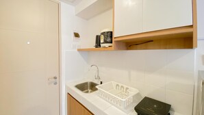 A kitchen with a white countertop, a stainless steel sink, a white plastic basket, and a black induction cooktop. - Warm And Simply Look Studio Apartment At Tokyo Riverside Pik 2 (Teluknaga)