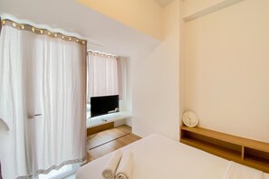Une chambre d’hôtel avec un lit, un téléviseur posé sur un meuble, une étagère en bois et une fenêtre avec des rideaux.