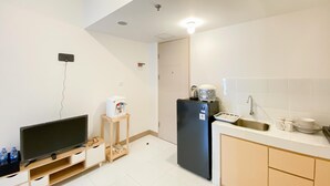 A compact kitchen with a TV, a refrigerator, a sink, and a small table. - Homey And Comfortable 2Br At Tokyo Riverside Pik 2 Apartment (Jakarta)